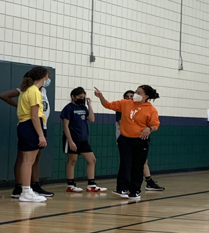 PUT ME IN, COACH Janelle Sterling (in orange) gives instructions during a huddle at basketball practice. Greenhills is Sterlings first varsity head coaching position. She has coached at almost all levels including recreational basketball, middle school, junior varsity, and has been a varsity assistant coach.