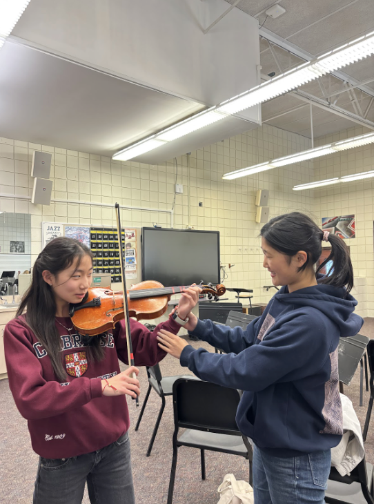 THE ART OF ADJUSTMENT Mentor Stella Kim assists her mentee, Amelia Lou, in playing the viola in the orchestra room. Stella and Amelia feel they have already made a lot of progress from the few times they’ve met. “This program has a very good way of bringing and uniting the middle school and high school students together,” said Goodell.